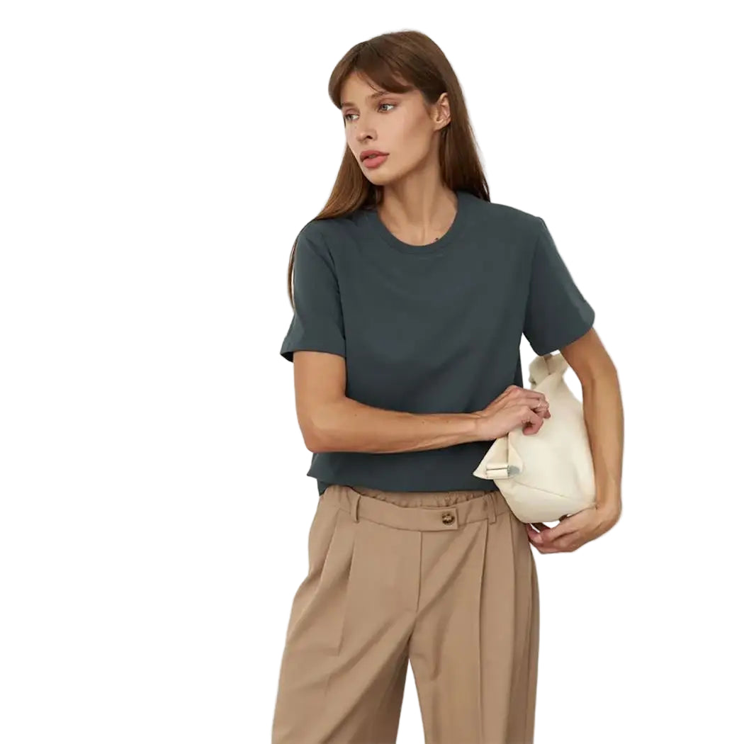 Woman wearing a dark green t-shirt and beige pants, holding a white handbag on a white background